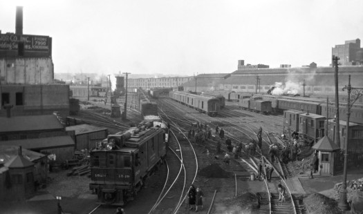 This image shows the New York Central Railroad's West Side Yard in Manhattan from the perspective of 11th Avenue and 31st Street. The locomotive in the foreground is a GE 3-power boxcab. In the distance, one of the Shay steam locomotives used on industrial street trackage is visible. Photograph by Donald W. Furler. Furler-23-006-01; © 2017, Center for Railroad Photography and Art