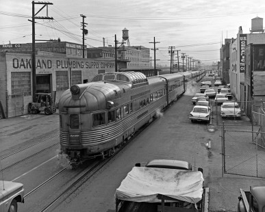 Western Pacific's <i>California Zephyr</i> departs Oakland, California, as it heads through a canyon of industry along 3rd Street on February 1, 1968. Observation-dome car "Silver Penthouse" brings up the rear of the eastbound <i>Zephyr</i> as it navigates a landscape dominated by building supply and paper warehouses under a looming "Safeway" water tower. This classic street running scene illustrates the train's use of steam heat, an abundance of "vintage" cars, and the world as we knew it before the advent of Amtrak and containerized freight. 

Read more about the <a href="http://www.railphoto-art.org/awards/2017-awards/" rel="nofollow">2017 John E. Gruber Creative Photography Awards Program</a>.