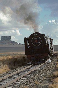 Eastbound South African Railways 25NC-class steam locomotive at Sekonyela, a railroad siding in Orange Free State (present-day Free State), South Africa, on July 12, 1984. Photograph by Katherine Botkin. BOTKINK-113-KT-24, © 1984, Katherine Botkin.