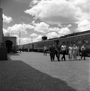 A group of young passengers walk along a platform at an unknown Atchison, Topeka & Santa Fe Railroad (AT&SF) station, on April 20, 1953. American soldiers on leave during the Korean War are seen in the background boarding a passenger car. Photograph by Wallace Abbey. © 2020, Center for Railroad Photography and Art, Abbey-01-113-08