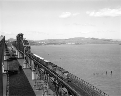 Union Pacific Railroad diesel locomotive no. 3006 leads westbound freight on Southern Pacific Railroad trackage over the Benicia–Martinez Bridge on March 30, 1971. The bridge connects Benicia and Martinez, California. Photograph by Victor Hand. Hand-UP-64-260.JPG