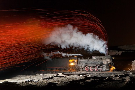 In Sandaoling, China, a JS steam locomotive emits hot ash in the exhaust made visible with the lack of lights at night.  A single strobe flash is used to illuminate the locomotive itself.
