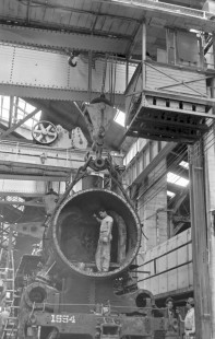 National Railways of Mexico steam locomotive no. 1554 is hoisted by crane in at shop at Aguascalientes, State of Aguascalientes, Mexico on September 12, 1961. A worker stands in the locomotive's smoke box. Rose-01-198-09; Photograph by Ted Rose,  © 2015, Center for Railroad Photography and Art