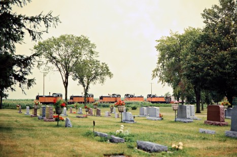 Westbound Milwaukee Road freight train passing cemetery in Spring Grove, Minnesota, on July 20, 1976. Photograph by John F. Bjorklund, © 2016, Center for Railroad Photography and Art. Bjorklund-65-08-09