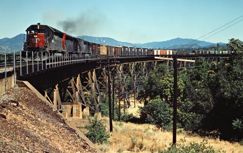 Westbound Southern Pacific Railroad freight train passing Sacramento River in Redding, California, on June 23, 1984. Photograph by John F. Bjorklund, © 2016, Center for Railroad Photography and Art. Bjorklund-86-21-03