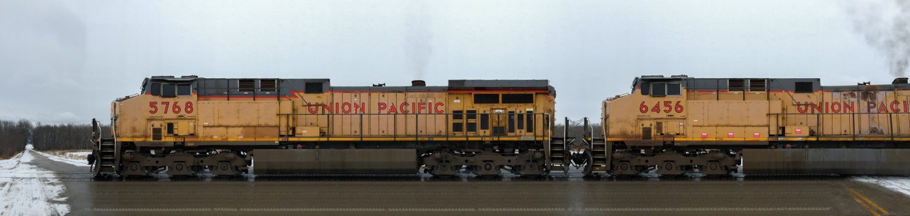 Photographer's notes: Union Pacific coal train in the town of Wilson, Sheboygan County, Wisconsin, on November 28, 2014. After playing around making standard panoramic photographs for a while, I thought I'd try a different tactic. Instead of moving the camera (phone), why not try locking the camera into a fixed position, and let the subject move on its own? You can see where this is going: set the phone up on a tripod next to the tracks, and wait for a train to pass. The concept is not unlike scanning a document on a gigantic photocopier. This entry depicts a loaded Union Pacific coal train on the Shoreline Subdivision, approaching its final destination of Sheboygan, Wisconsin. The typical operating pattern is for the train to stop south of Stahl Road, a rural crossing on the outskirts of Sheboygan. There the conductor would alight, the train would move northward, and the conductor would cut the train in half. The train moving slowly over the grade crossing is an essential characteristic in capturing the image properly. 

Read more about the <a href="http://www.railphoto-art.org/awards/2016-awards/" rel="nofollow">2016 John E. Gruber Creative Photography Awards Program</a>.