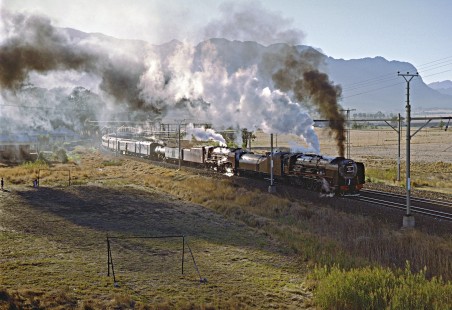 Two South African Railways steam locomotives lead a special passenger train through the village of Artois on April 2, 1995, as a few local children watch from an adjacent soccer field. Photograph by Fred M. Springer, © 2016, Center for Railroad Photography and Art. Springer-So.Africa-NOR-SWE-06-24