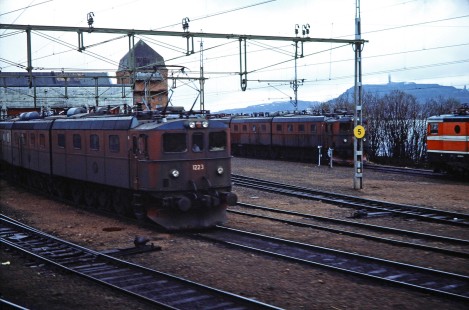 Swedish State Railways electric locomotive no. 1223 moves along a track exiting the train station with other trains also on a nearby track in Kiruna, Norrbotten, Sweden on June 5, 1989. This photograph is taken as the photographer travels the areas of Boden, Sweden and Nordland, Norway. Photograph by Fred M. Springer, © 2014, Center for Railroad Photography and Art. Springer-Scan-Swiss-York-06-23