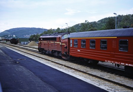 Norwegian State Railways diesel locomotive moves a "1.Klasse" passenger car along the track at Mosjøen, Nordland, Norway on June 7, 1989. This photograph is taken as the photographer travels the areas of Nordland and Sør-Trøndelag, Norway. Photograph by Fred M. Springer, © 2014, Center for Railroad Photography and Art. Springer-Scan-Swiss-York-08-24