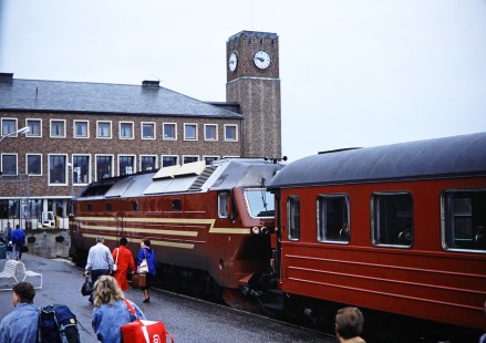 Norwegian State Railways diesel locomotive and passenger car wait as passengers move along the platform to the nearby station in Bodø, Nordland, Norway on June 7, 1989. This photograph is taken as the photographer travels the areas of Nordland and Sør-Trøndelag, Norway. Photograph by Fred M. Springer, © 2014, Center for Railroad Photography and Art. Springer-Scan-Swiss-York-08-33
