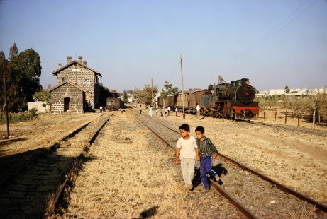 Syrian Railways 2-8-2 steam locomotive no. 263 waits at a station with a crowd of onlookers nearby in Daraa, Daraa, Syria on July 21, 1991. Photograph by Fred M. Springer, © 2014, Center for Railroad Photography and Art. Springer-Hedjaz-ZimZam(1)-11-05