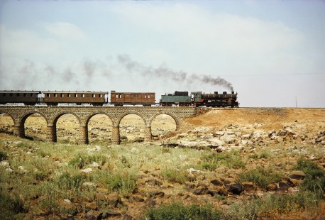 Syrian Railways 2-8-2 steam locomotive no. 263 crosses a bridge with passenger cars in Bosra, Daraa, Syria on July 21, 1991. Photograph by Fred M. Springer, © 2014, Center for Railroad Photography and Art. Springer-Hedjaz-ZimZam(1)-12-01