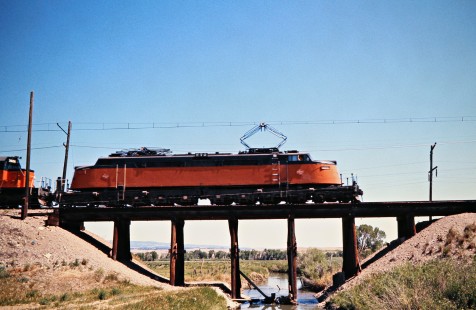 Eastbound Milwaukee Road "Little Joe" electric locomotive crossing bridge at Martinsdale, Montana, on July 8, 1973. Photograph by John F. Bjorklund, © 2016, Center for Railroad Photography and Art. Bjorklund-63-17-05