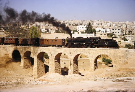 Hedjaz Jordan Railway 4-6-2 steam locomotive no. 82 pulling passenger cars across a small bridge in Amman, Jordan, on July 16, 1991. Photograph by Fred M. Springer, © 2014, Center for Railroad Photography and Art. Springer-Hedjaz-ZimZam(1)-04-32