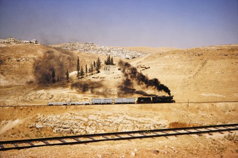 Hedjaz Jordan Railway 2-8-2 steam locomotive no. 71 with two boxcars and two flatcars moving across open desert in Amman, Jordan, on July 15, 1991. Photograph by Fred M. Springer, © 2014, Center for Railroad Photography and Art. Springer-Hedjaz-ZimZam(1)-03-31