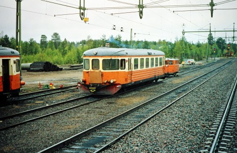NVHJ diesel railcar no. 3802 moves along the track away from a road crossing surrounded by other cars in  Nattavaara, Sweden on June 5, 1989. This photograph is taken as the photographer travels the areas of Boden, Sweden and Nordland, Norway. Photograph by Fred M. Springer, © 2014, Center for Railroad Photography and Art. Springer-Scan-Swiss-York-06-37