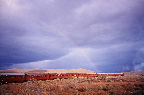 A long train of South African Railway passenger cars pass a clear view of a rainbow in Western Cape, South Africa, on March 19, 1995. Photograph by Fred M. Springer, © 2014, Center for Railroad Photography and Art. Springer-So.Africa(1)-10-17