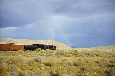 South African Railway 4-8-4 steam locomotive no. 3501 moves along a hilly landscape and underneath a single rainbow in Western Cape, South Africa, on March 19, 1995. Photograph by Fred M. Springer, © 2014, Center for Railroad Photography and Art. Springer-So.Africa(1)-10-09