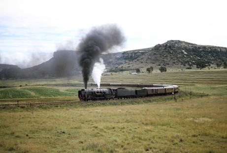 The surrounding bluffs and farm fields highlight South African Railway 4-8-4 steam locomotive no. 3410 traveling on a horseshoe curve in Clocolan/Modderpoort, Free State, South Africa, on March 26, 1995. Photograph by Fred M. Springer, © 2014, Center for Railroad Photography and Art. Springer-So.Africa(1)-21-29