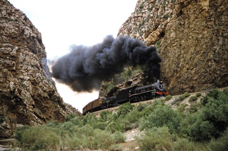 South African Railway 4-8-2 steam locomotive no. 1882 travels between two rocky bluffs in Toorwater, Western Cape, South Africa, on March 24, 1995. Photograph by Fred M. Springer, © 2014, Center for Railroad Photography and Art. Springer-So.Africa(1)-17-06
