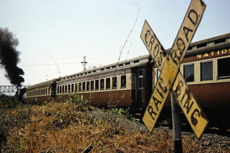 A close-up of railroad crossing sign as a National Railways of Zimbabwe Garratt steam locomotive and passenger train pass by the marker in Hwange, Matabeleland, Zimbabwe, on August 6, 1991. Photograph by Fred M. Springer, © 2014, Center for Railroad Photography and Art. Springer-Hedjaz-ZimZam(1)-24-01