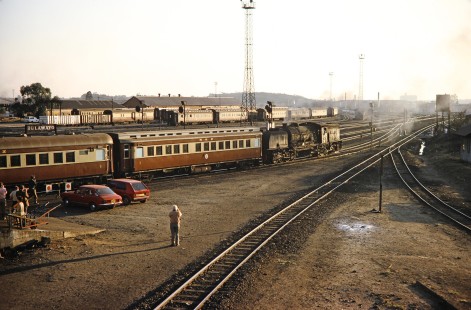 A rail photographer sets up to get a ideal picture of the yard in Bulawayo, Zimbabwe, on August 2, 1991, where a Garratt steam locomotive waits with a National Railways of Zimbabwe passenger train. Photograph by Fred M. Springer, © 2014, Center for Railroad Photography and Art. Springer-Hedjaz-ZimZam(1)-19-38