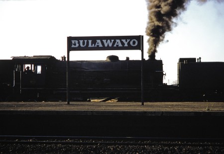 The platform signpost for the station in Bulawayo, Zimbabwe, on August 1, 1991, with a Garratt steam locomotive behind. Photograph by Fred M. Springer, © 2014, Center for Railroad Photography and Art. Springer-Hedjaz-ZimZam(1)-17-31