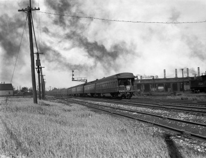 The Wabash Railroad's  (WAB) <i>Detroit Arrow</i> passenger train (note the conductor on the back platform) passing a roundhouse in an unidentified rail yard, unknown date. Photograph by Robert A. Hadley. © 2016, Center for Railroad Photography and Art