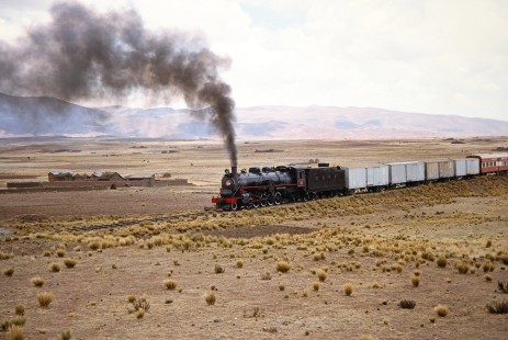 Empresa Nacional de Ferrocarriles Bolivia 2-10-2 steam locomotive no. 704 is seen against an arid landscape of mountains and plateaus in Tiwanaku, Western Bolivia, Bolivia, on September 30, 1992. Photograph by Fred M. Springer, © 2014, Center for Railroad Photography and Art. Springer-ARG-PA-CHI-BO2-12-07