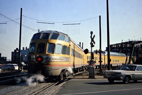 One of the Milwaukee Road's Skytop observation-lounge cars brings up the rear of the <i>Morning Hiawatha</i> passenger train as it departs Milwaukee, Wisconsin, for Chicago on Saturday, November 12, 1966. The car is passing under "tell tales" (hanging wires used to warn workers riding car tops) for the Menomonee River drawbridge, visible at right. Photograph by Thomas F. McIlwraith, McIlwraith-01-005-14, © 2018, Center for Railroad Photography & Art, <a href="http://www.railphoto-art.org" rel="noreferrer nofollow">www.railphoto-art.org</a>