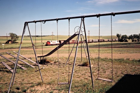 Northbound Soo Line Railroad freight train passing a playground at Baldwin, North Dakota, on July 7, 1980. Photograph by John F. Bjorklund, © 2016, Center for Railroad Photography and Art. Bjorklund-83-23-03