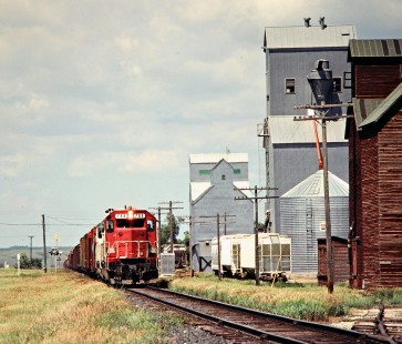 Eastbound Soo Line Railroad freight train passing grain elevators at Carpio, North Dakota, on July 6, 1980. Photograph by John F. Bjorklund, © 2016, Center for Railroad Photography and Art. Bjorklund-83-07-01
