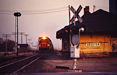 Soo Line Railroad freight train approaching crossing with a Griswold crossing signal at Brooten, Minnesota, on April 17, 1981. Photograph by John F. Bjorklund, © 2016, Center for Railroad Photography and Art. Bjorklund-83-18-18