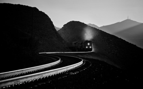Following the best course plotted by the line’s surveyors, this Union Pacific train is passing through Sloan, Nevada, on its climb west out of the Las Vegas valley in 2014. Read more at <a href="http://www.railphoto-art.org/2015-awards" rel="nofollow">www.railphoto-art.org/2015-awards</a>