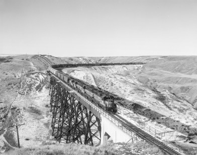 Milwaukee Road diesel locomotive no. 556 crosses Red Coulee trestle bridge with eastbound freight on February 24, 1980. Photograph shot near Salem, Montana, by Victor Hand. Hand-MILW-67-162