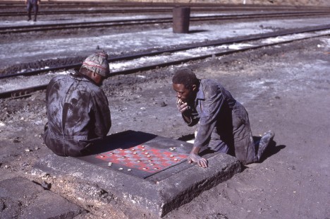 National Railways of Zimbabwe steam fitters playing bottle cap checkers at the Bulawayo steam shed, on July 27, 1984. At this time, the shed serviced 105 Garratt steam locomotives, which operated from Bulawayo, north to Victoria Falls, and south to West Nicholson.

Read more about the <a href="http://www.railphoto-art.org/awards/2019-awards/" rel="noreferrer nofollow">2019 John E. Gruber Creative Photography Awards Program</a>.