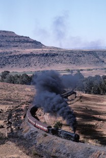 South African Railways 25NC-class steam locomotive no. 3408 leads passenger train north of Owanty Station in Setsoto, Orange Free State (present-day Free State), South Africa, on May 27, 1985. Photograph by Katherine Botkin. BOTKINK-113-KT-66, © 1985, Katherine Botkin.