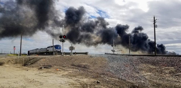 Amtrak's San Joaquin No. 717 at the Avenue 112 and Highway 43 crossing in Angiola, California, on March 15, 2020. The manure compost piles at the local dairy had caught fire and created a dramatic smoke display against the storm clouds. © Laura Lawrence