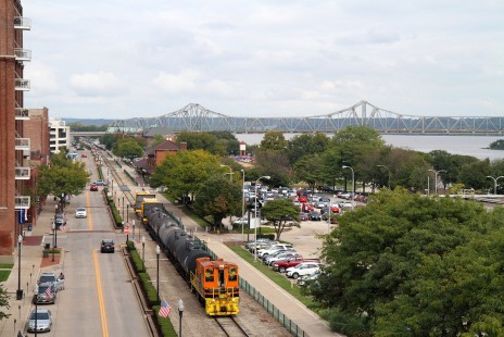 A Tazewell & Peoria Railroad train ambles along the downtown Peoria, Illinois riverfront on its return to the railroad's classification yard in Creve Coeur after working local industries. Trailing SW1500 #1521 are five tank cars from PMP Fermentation Products and two flatcars of heavy mining truck equipment from Komatsu America Corporation. © Brian Carlson