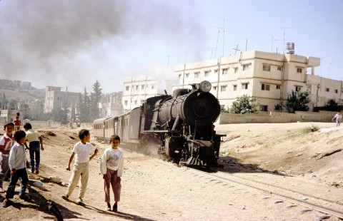 A group of young boys gather near the track of the Hedjaz Jordan Railway (HJR), in Amman, Jordan, on July 15, 1991. HJR steam locomotive no. 71 pulls a passenger train along the outskirts of the city. Photograph by Fred Springer. © 2020, Center for Railroad Photography and Art, Springer-Hedjaz-ZimZam(1)-02-27