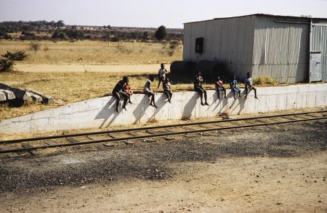 A group of children sit on a concrete berm and watch the passing trains along a National Railways of Zimbabwe (NRZ) mainline in Mbalabala, Matabeleland, Zimbabwe, on August 3, 1991. Photograph by Fred Springer. © 2020, Center for Railroad Photography and Art, Springer-Hedjaz-ZimZam(1)-20-21