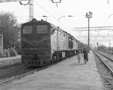 Soviet Railways (SZD) diesel locomotive 2TE-10L-2224 pauses in Ekibastuz, Pavlodar, Kazakhstan, on July 23, 1995. As a mother and daughter pass by the engine, the little girl looks up at the crew in the cab. Photograph by Victor Hand, Hand-SZD-265-20