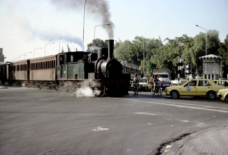 General Establishment of Syrian Railways (CFS) steam locomotive no. 130 leads a passenger train through a traffic intersection in Damascus, Syria, on July 20, 1991. Photograph by Fred Springer. © 2020, Center for Railroad Photography and Art, Springer-Hedjaz-ZimZam(1)-09-27