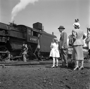 A father and son get a close look at Chicago and North Western Railroad (CNW) steam locomotive no. 2397, while another family admires from afar. Both families were part of a National Railway Historical Society fan trip from Milwaukee to Green Bay, Wisconsin, on May 25, 1952.  Photograph by Wallace Abbey. © 2020, Center for Railroad Photography and Art, Abbey-01-149-06