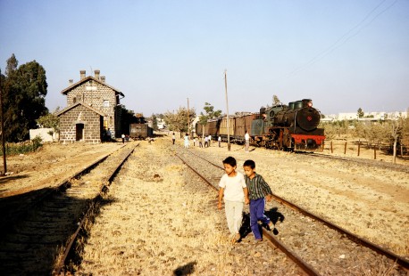 Two boys scurry across some tracks while General Establishment of Syrian Railways (CFS) steam locomotive no. 263 prepares to pull a passenger train out of Daraa, Syria, on July 21, 1991. Photograph by Fred Springer. © 2020, Center for Railroad Photography and Art, Springer-Hedjaz-ZimZam(1)-11-05