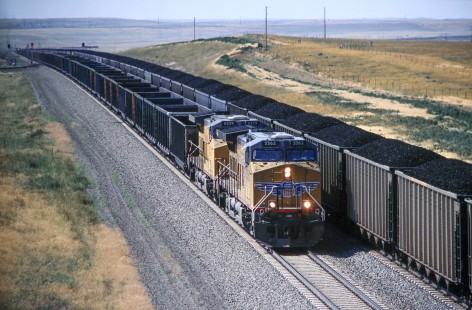 Union Pacific Railroad locomotive no. 5562 and no. 6529 with northbound empty hopper train pass loads near south end of loadout structures line to Bill, an unincorporated community in Converse county Wyoming, in  August of 2005. Photograph by J. Parker Lamb. Lamb-03-041-16.JPG; © 2016, Center for Railroad Photography and Art
