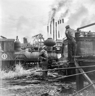 A Black railroader converses with another worker amid the Argent Lumber Company's smoky yard just outside of Hardeeville, South Carolina, in the early months of 1956. Photograph by Jim Shaughnessy. © 2021, Center for Railroad Photography and Art. Shaughnessy-N-ARGENT-0021-2