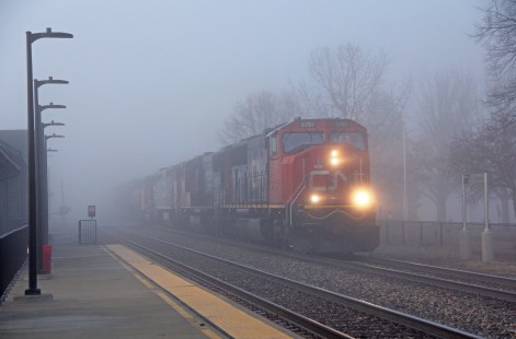 A northbound Canadian National manifest freight breaks out of the gloom by the Amtrak station in Rantoul, IL. February 27, 2021