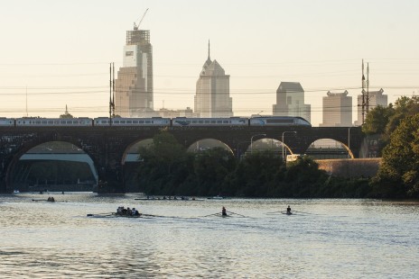 <i>Acela Express</i> train 2103 crosses the Schuylkill River in Philadelphia, Pennsylvania, while rowers practice at dawn on September 18, 2007. Photograph by Scott Lothes, president and executive director of the Center for Railroad Photography & Art