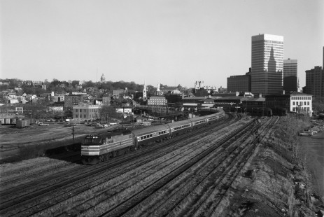 On Christmas Eve, 1976, an Amtrak train from Boston to Washington pulls out of Providence, Rhode Island. The shadow of the iconic Industrial National Bank Building falls on the skyscraper in the background at right, while the Rhode Island State House is visible on the horizon at left. Today this scene is greatly changed following electrification of the railway and construction of the Providence Place shopping mall in the 1990s. Photograph by Victor Hand, collection of the Center for Railroad Photography & Art, Hand-AM-59-093